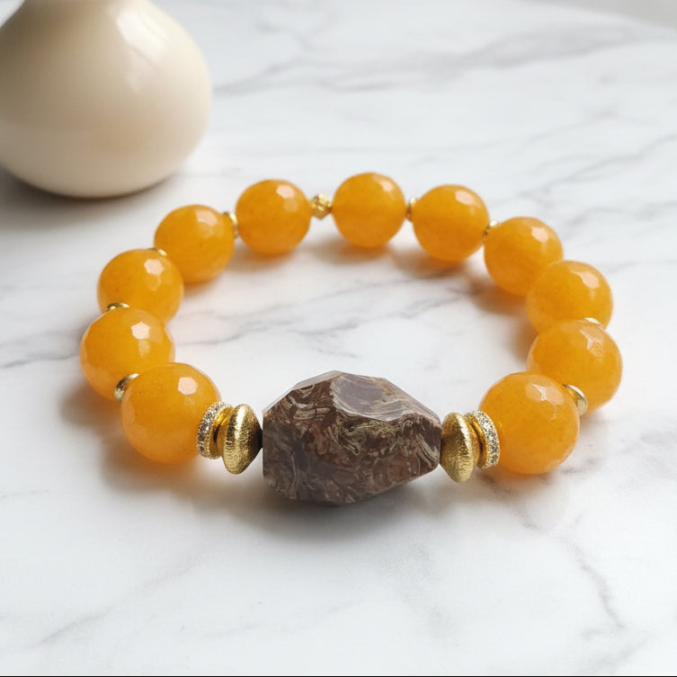 A wrist bracelet with a series of dark gold beads and a brown crystal or stone in the center on a neutral background.