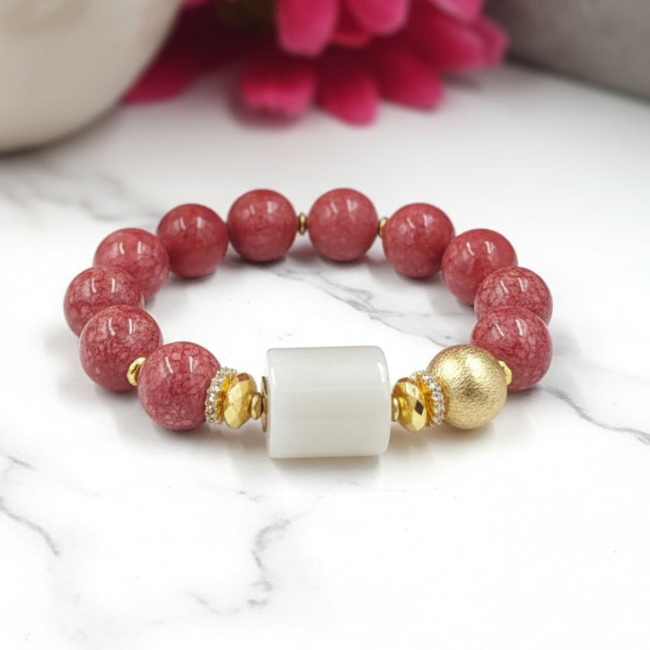 A raspberry red and pink beaded bracelet with gold accents and a white ceramic bead cap.