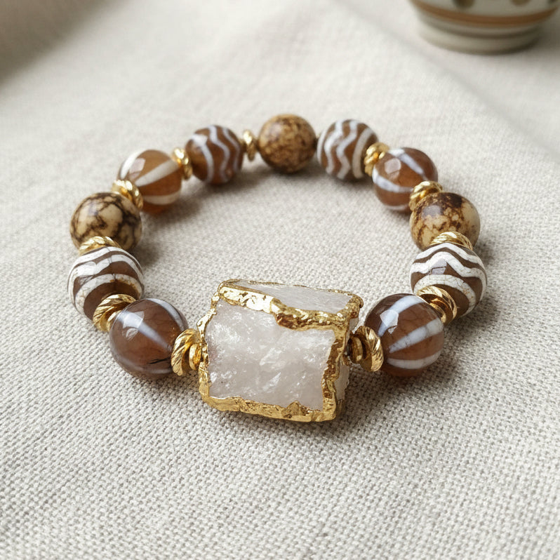 A multicolored beaded bracelet with a gold trimmed clear quartz centerpiece, displayed against a natural background.