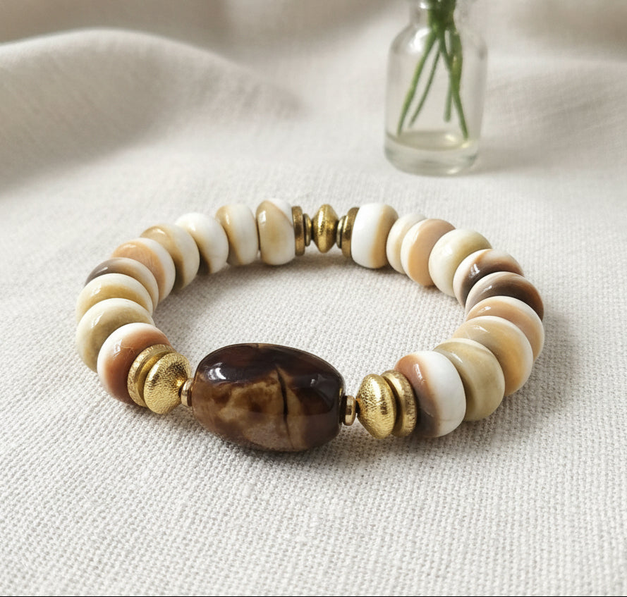 A multicolored beaded bracelet with a variety of bead colors including white, beige, brown, and black, featuring a tiger's eye bead, secured with gold-colored beads.