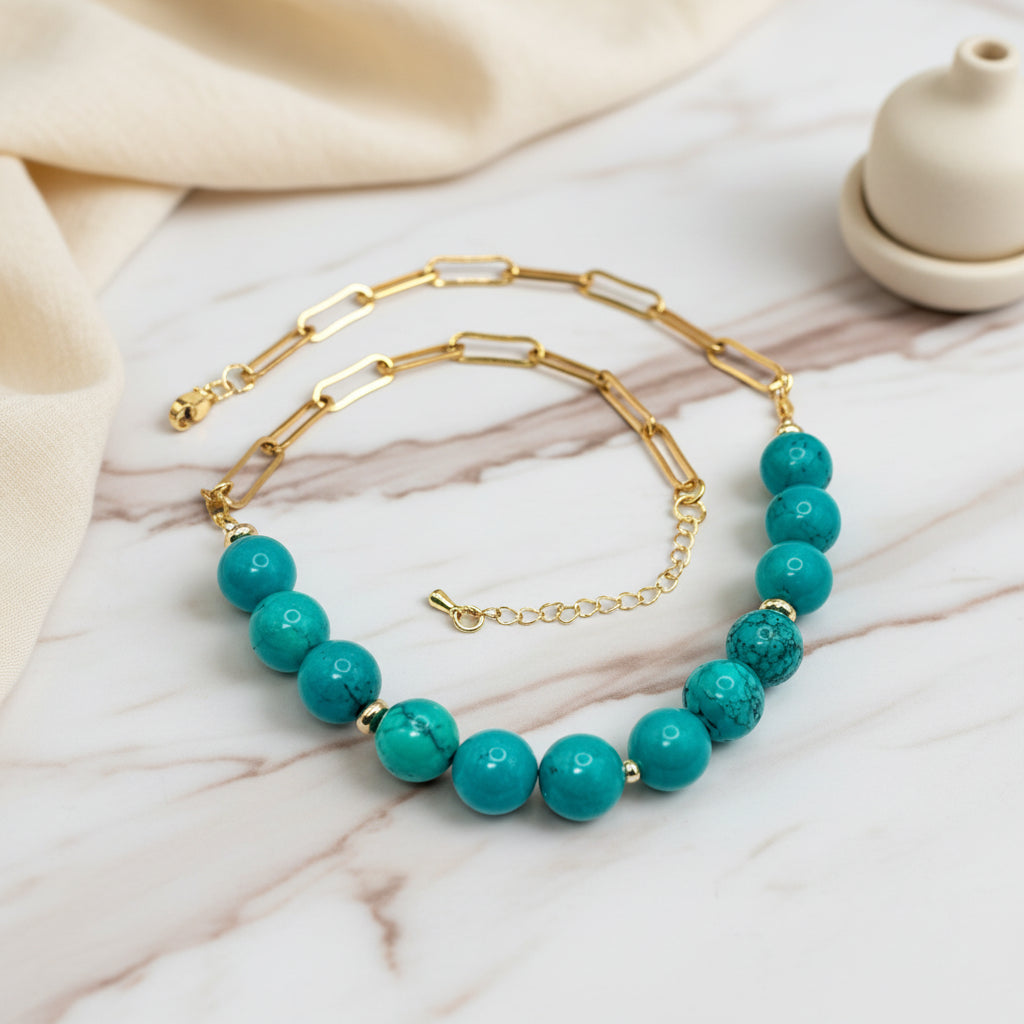Gold necklace with turquoise beads on a white surface with decorative elements.