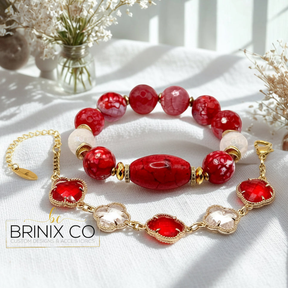 Bracelet set with red, clear and gold beads on a white surface with flowers in the background