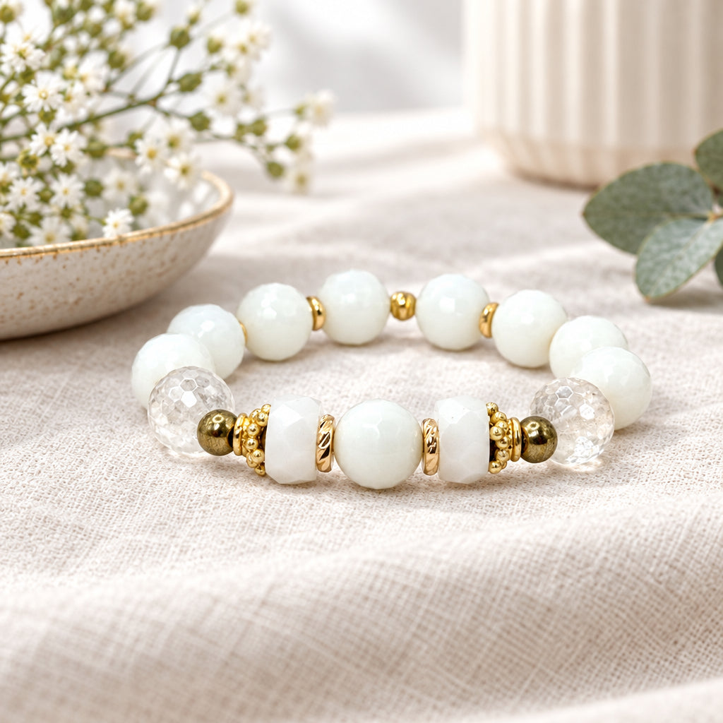 White beaded bracelet with gold accents on a linen surface with a decorative glass item in the background.