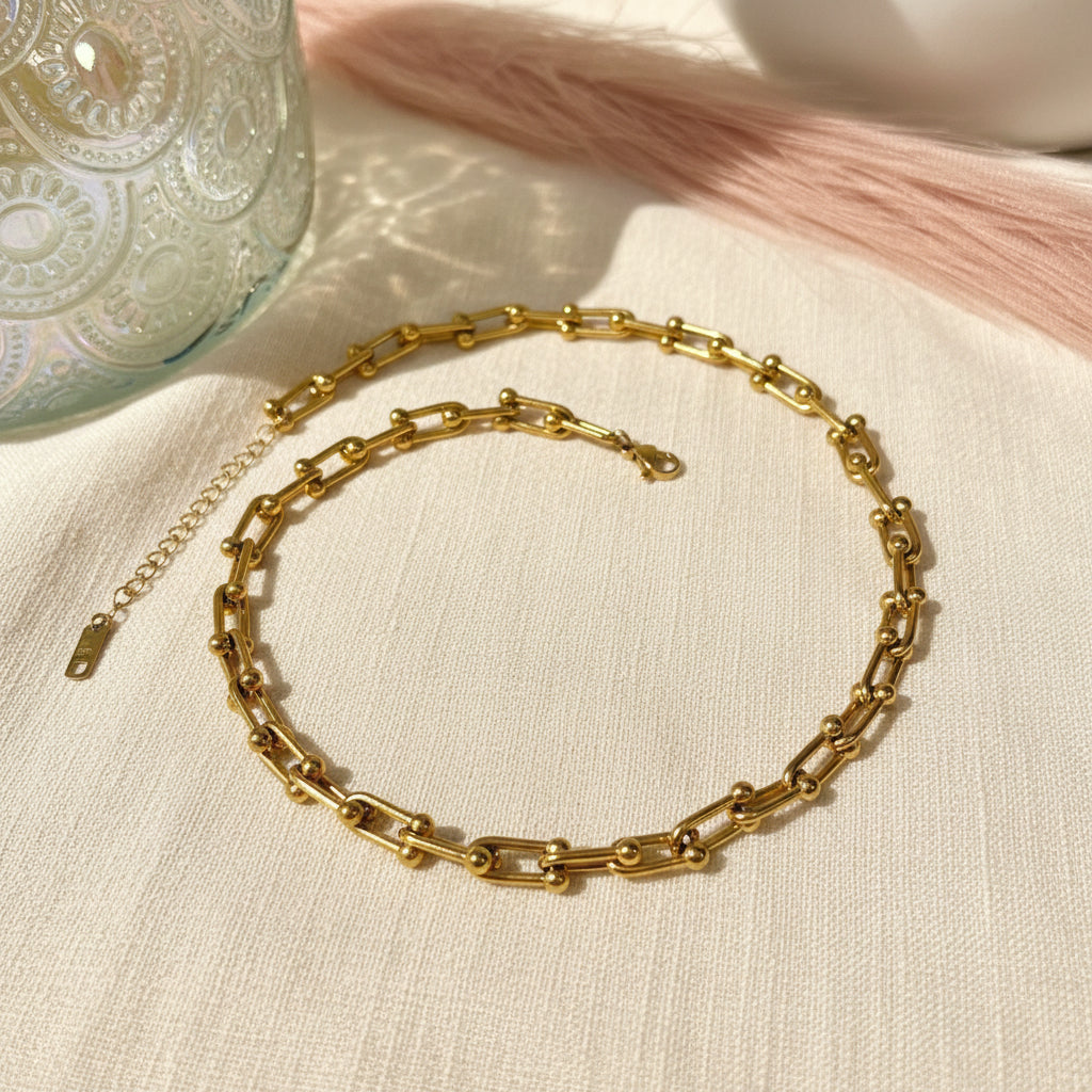 Gold chain necklace on a white surface with a decorative vase in the background