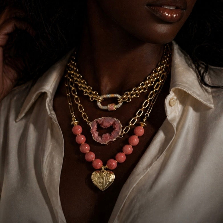 Close-up of a person wearing multiple necklaces with peach beads and gold chains.