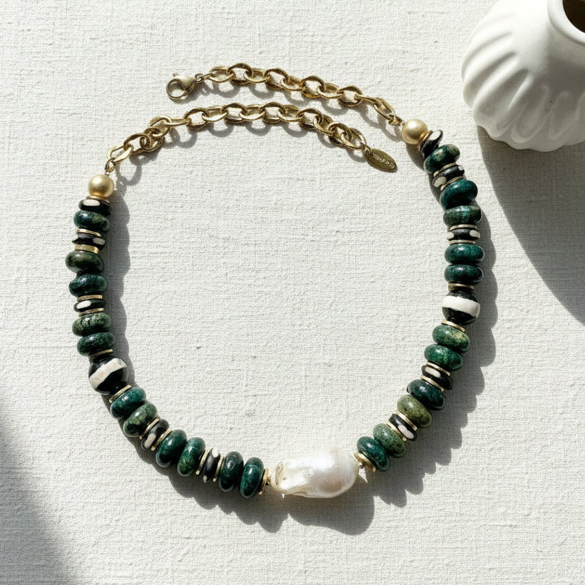 Green beaded necklace with a gold chain on a light gray surface