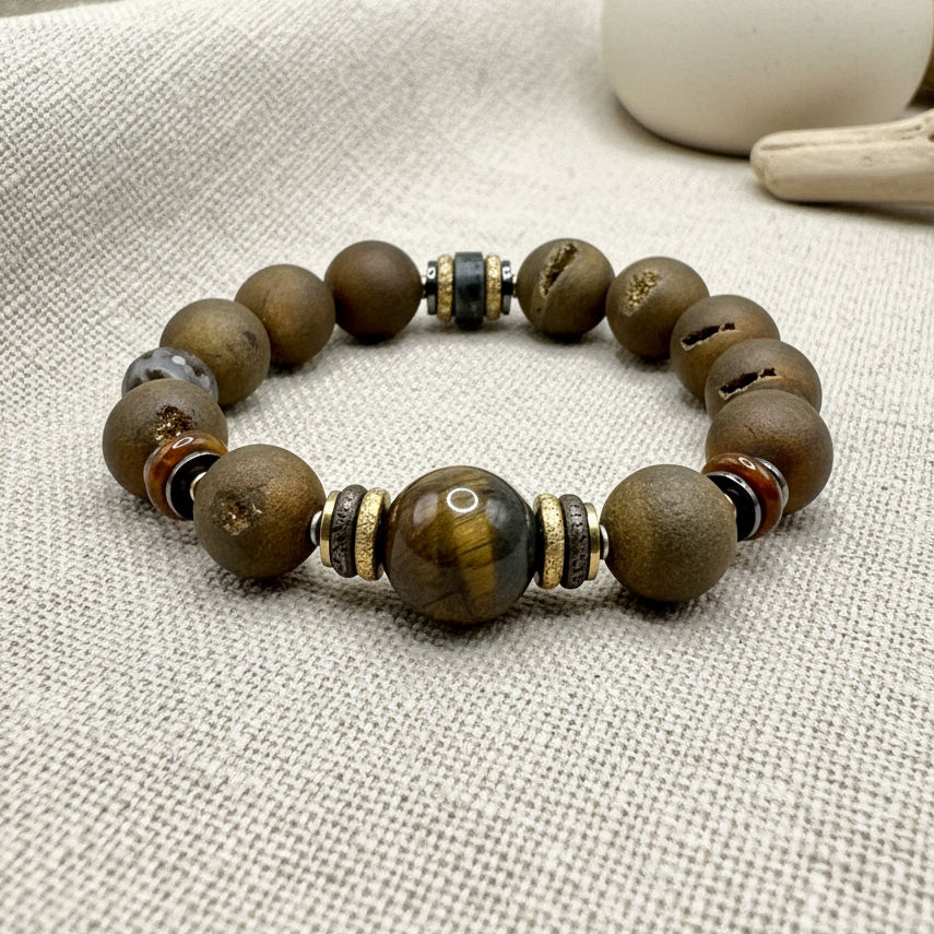 A gold-colored bracelet featuring round beads with a Tiger's Eye pattern and metallic accents on a white background.