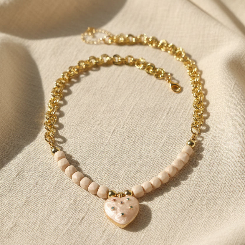 Necklace with heart-shaped pendant and beige beads on a white surface