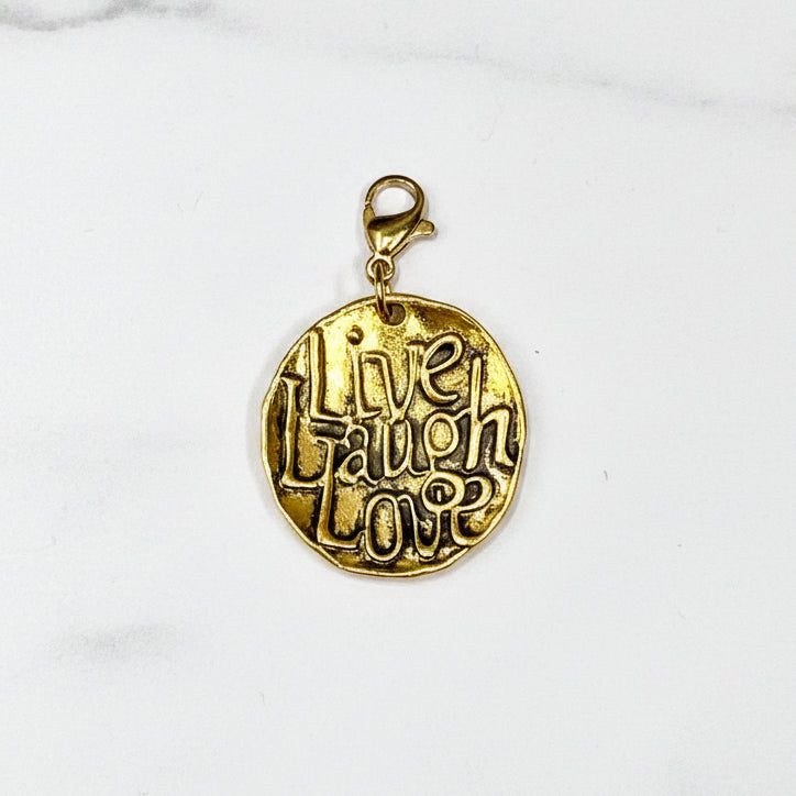 A gold-colored metal charm with the inscription 'LIVE LAUGH LOVE' on it, displayed against a neutral background.