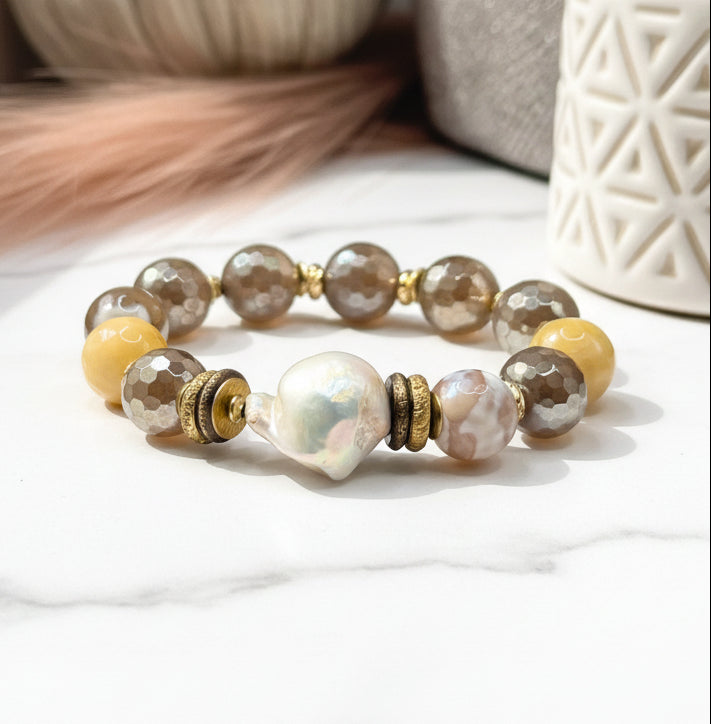 A bracelet with a mix of gray, yellow, and white beads, alongside gold-colored accents, displayed on a neutral surface.