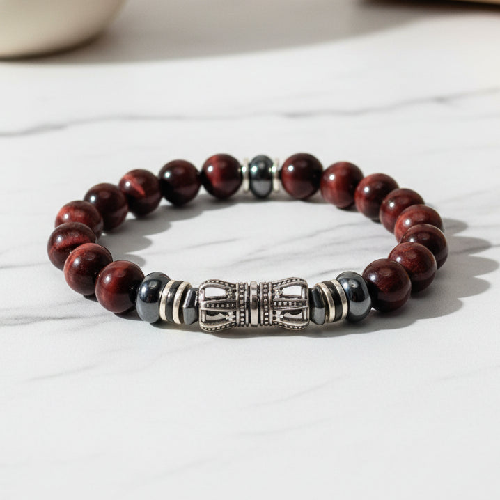 A bracelet with red tiger eye stones and a gold-colored clasp, displayed on a white surface with a textured background.