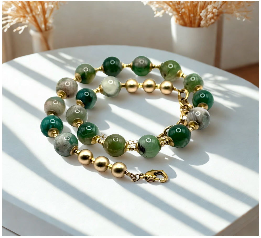 Green and gold beaded necklace on a white surface with a soft focus background