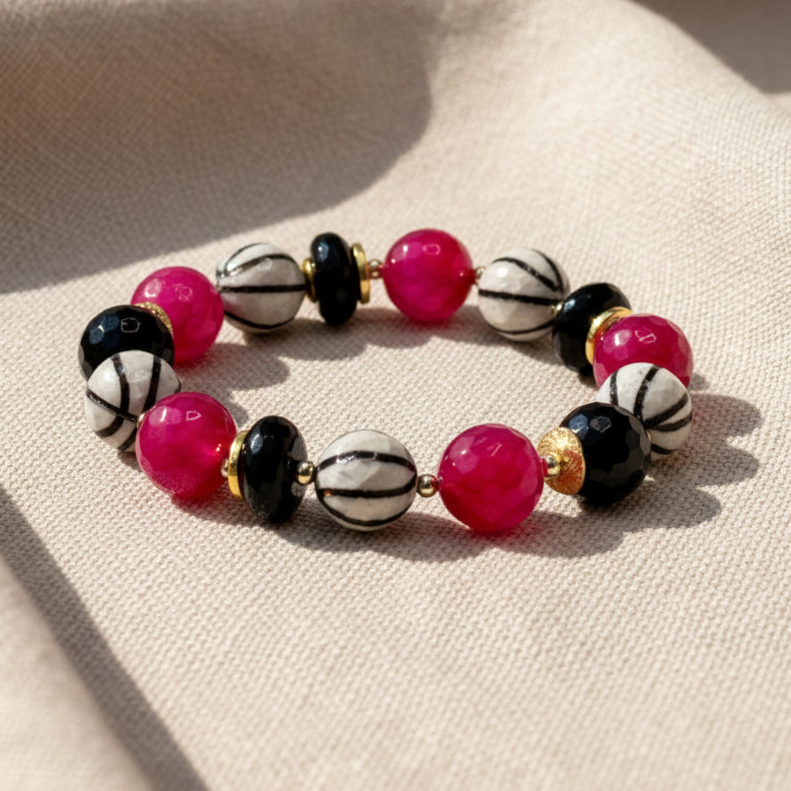 Colorful beaded bracelet on a white surface with pink decorative elements in the background