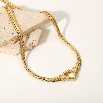 Gold herringbone chain necklace with a heart-shaped pendant on a off-white background