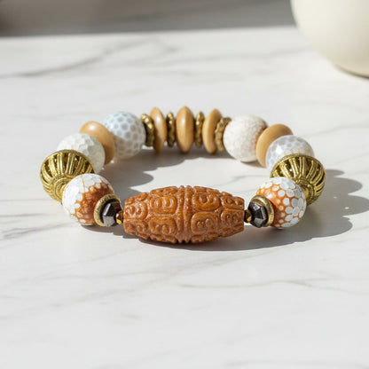 Beaded bracelet with gold, white, and brown beads on a dark surface