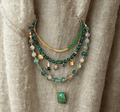 Stack of green and gold beaded necklaces on a textured beige fabric background