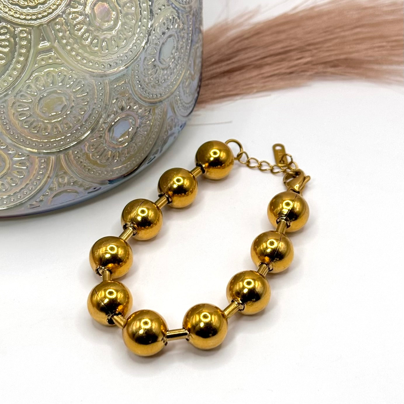 18k Gold plated ball chain bracelet on a white surface with a candle in the background.
