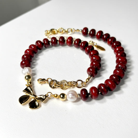 Beaded necklace with red jasper beads, gold accents, and pearl elements on a white background