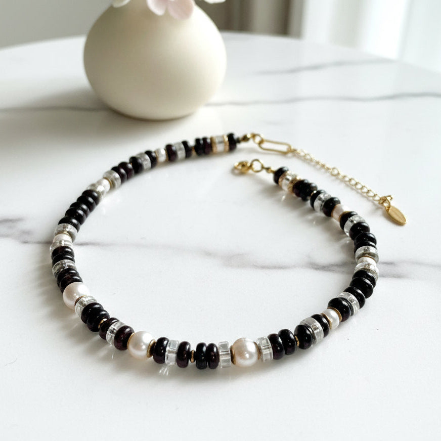 Necklace with garnet, fresh water pearl, and gold beads on a white background