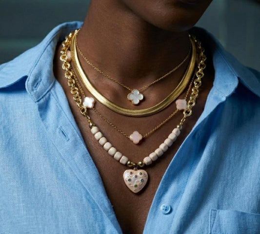 Person wearing multiple gold necklaces with heart and floral pendants on a blue shirt.