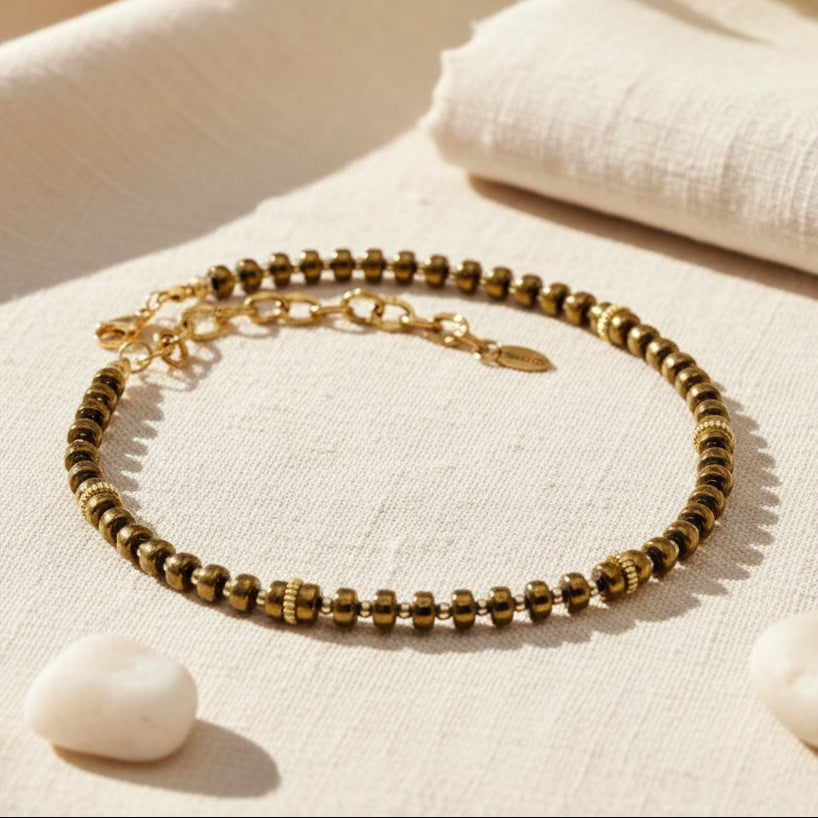 Gold beaded necklace on a white surface with a blurred background