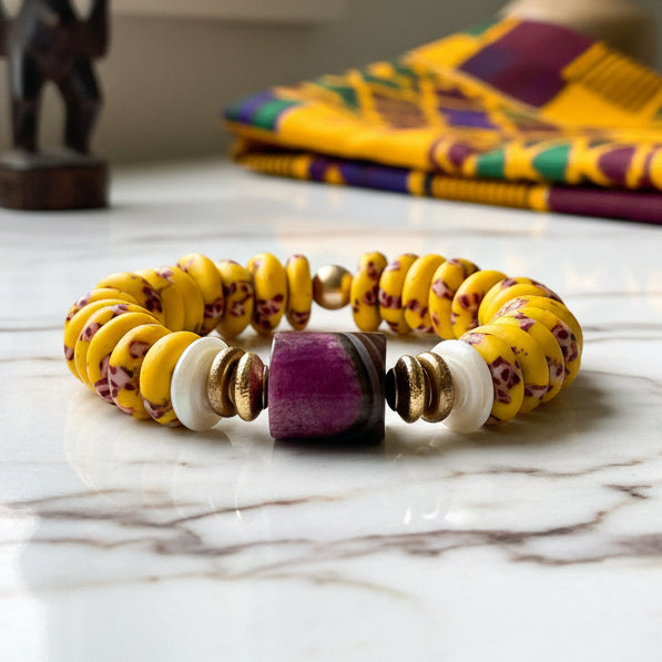 Yellow beaded bracelet with purple and gold accents on a white background