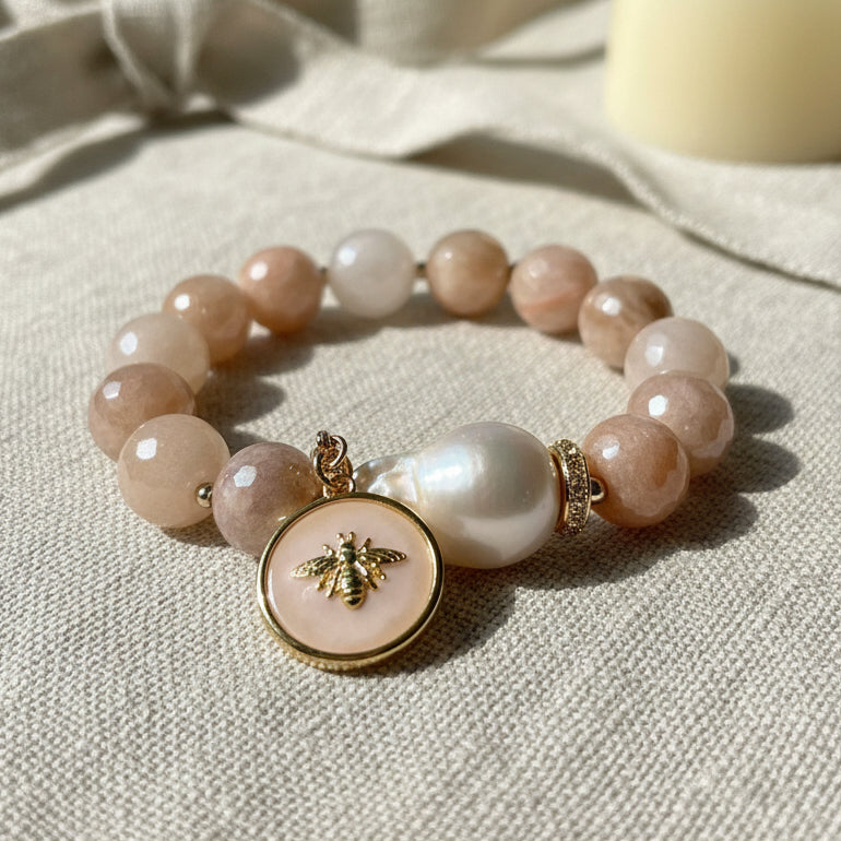 Bracelet with peach beads and a gold bee charm on a beige fabric background