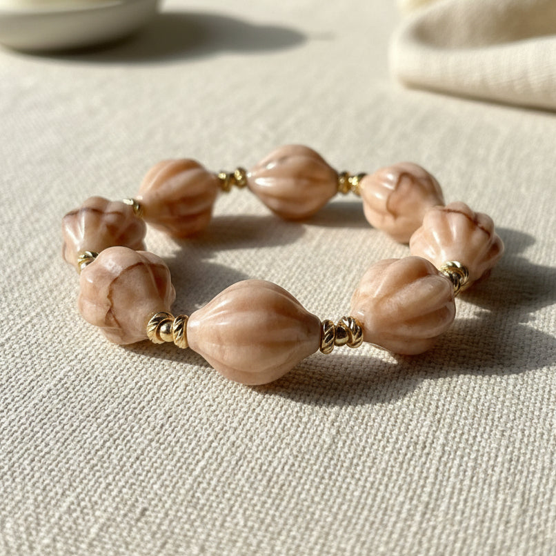 Peach shell shaped beaded bracelet with gold accents on a linen background