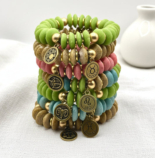 Stack of colorful beaded bracelets with zodiac charms on a light background