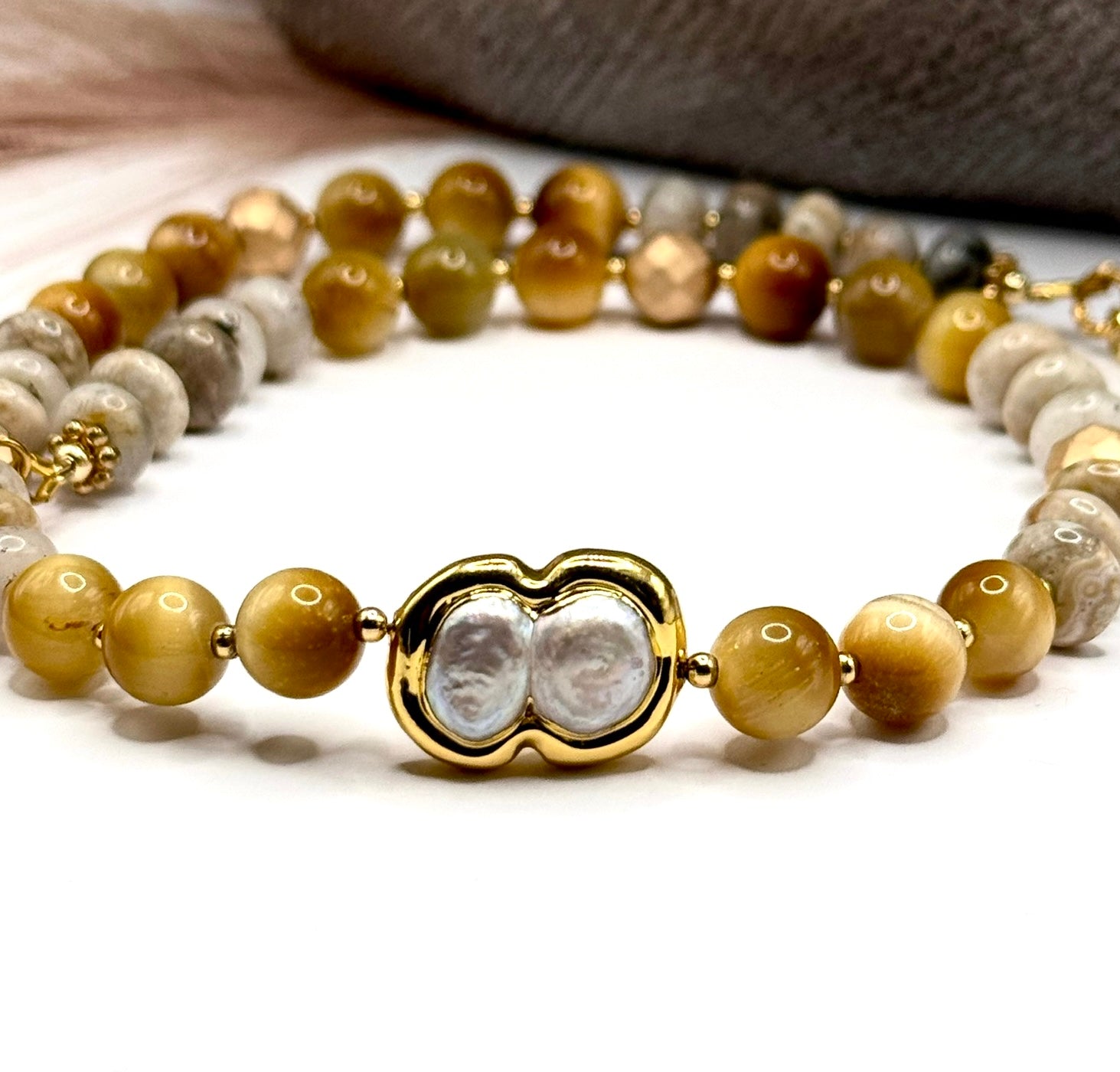 Close up of beaded necklace with gold tiger eye and jasper beads with focus on pearl centerpiece.